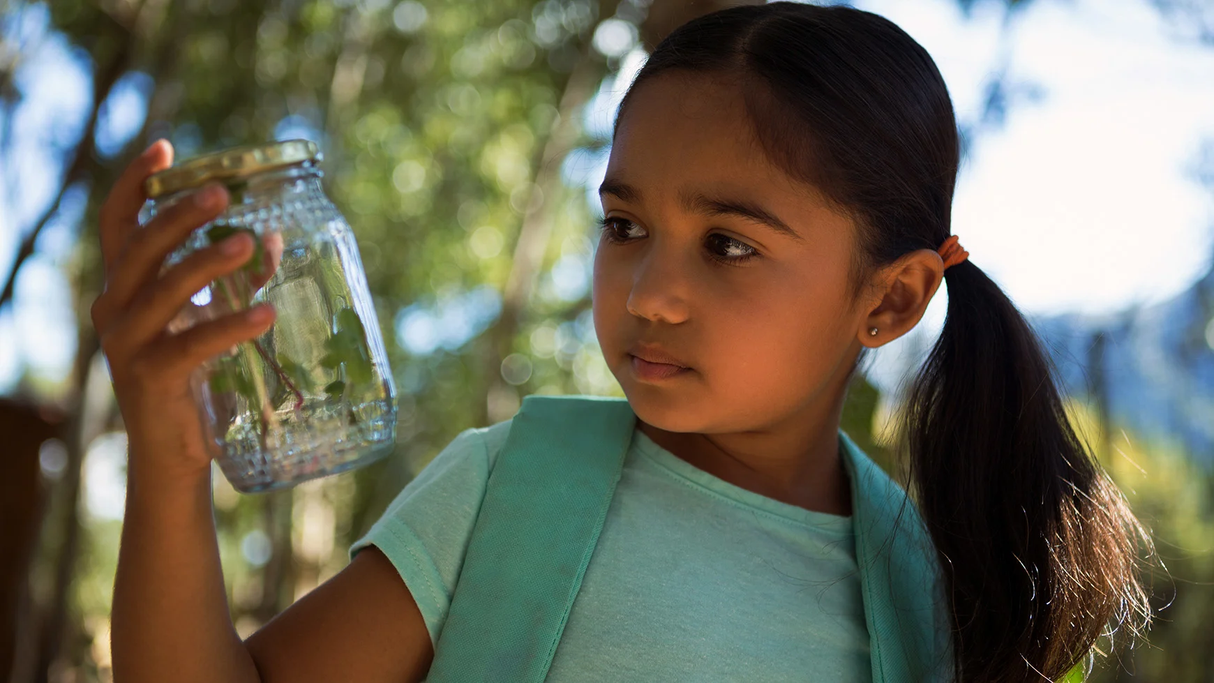 A girl looks at an insect she caught in a jar. 