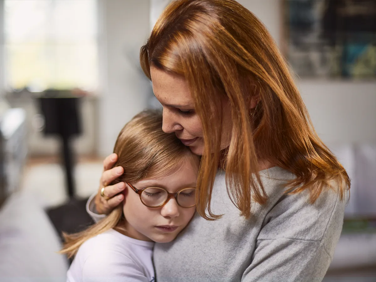 An adult hugs a child with glasses. 