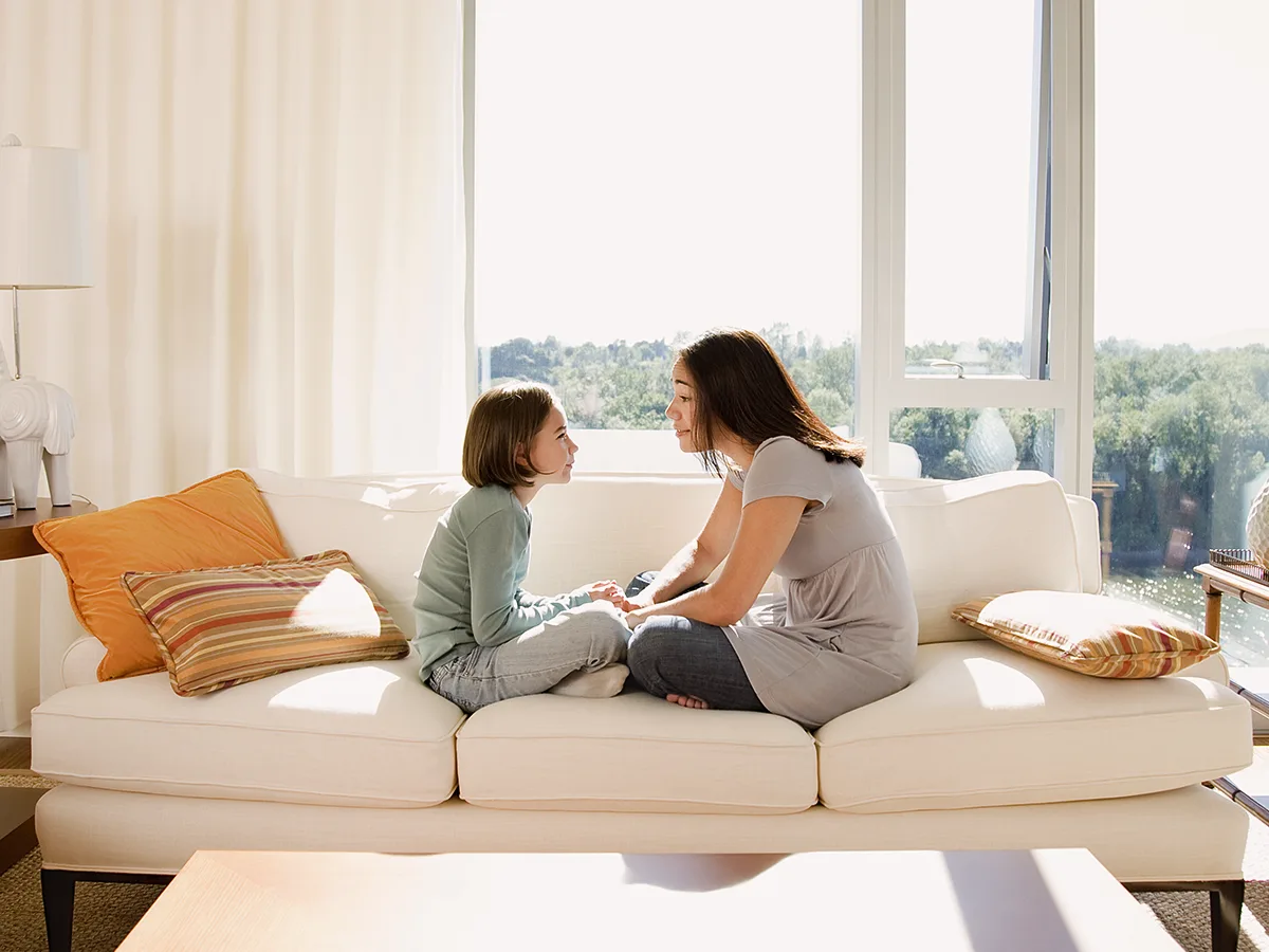Our Community Weighs In: Explaining ADHD to Your Child, mother talking to daughter sitting on a couch at home