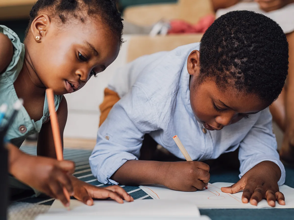 Two children writing on pieces of paper.  