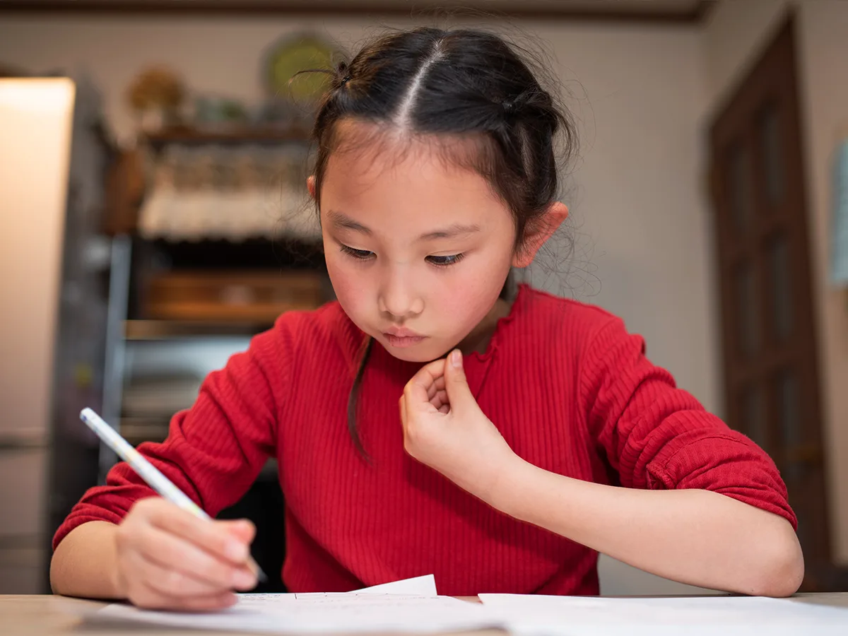 Una niña escribe con un lápiz sobre una hoja de papel.