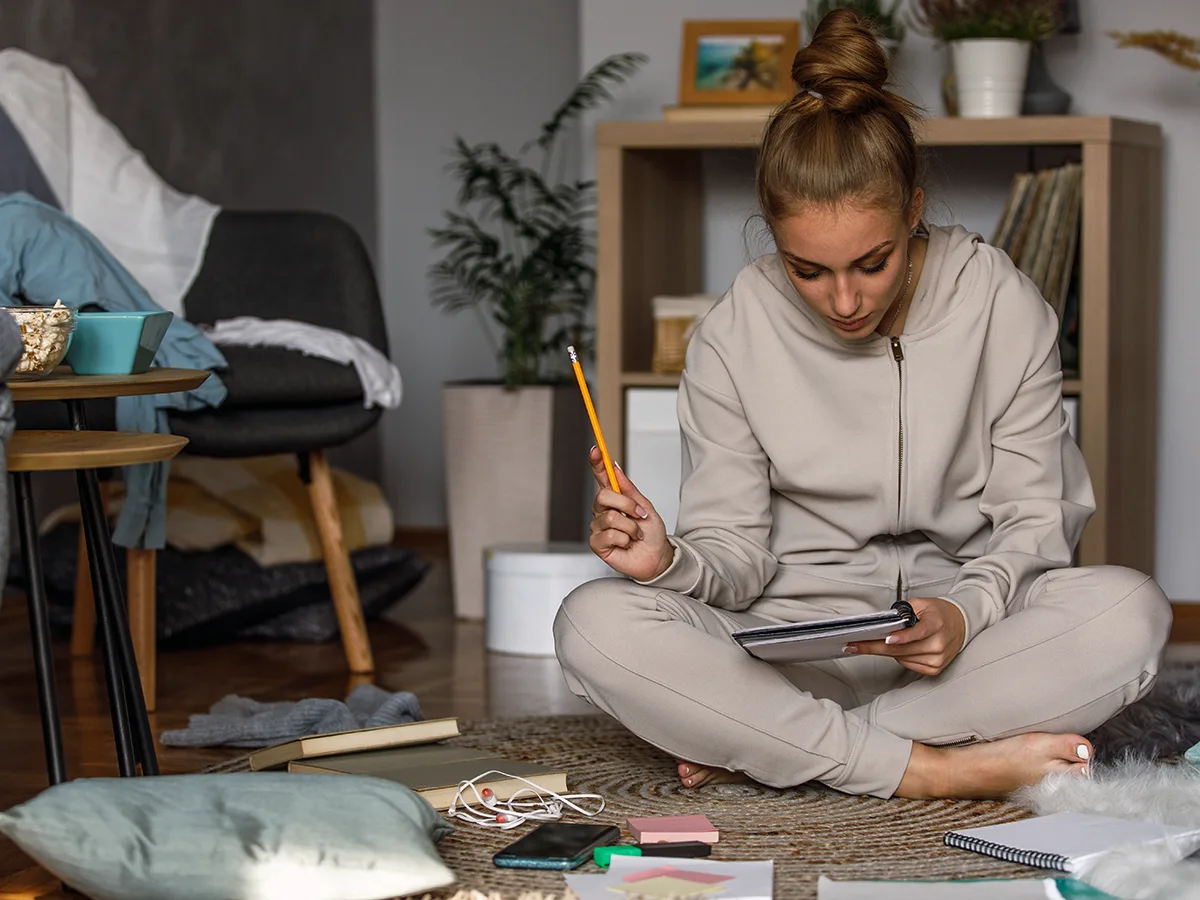 ADHD and Time Blindness. A young adult sits on the floor looking at a tablet surrounded by various papers. 