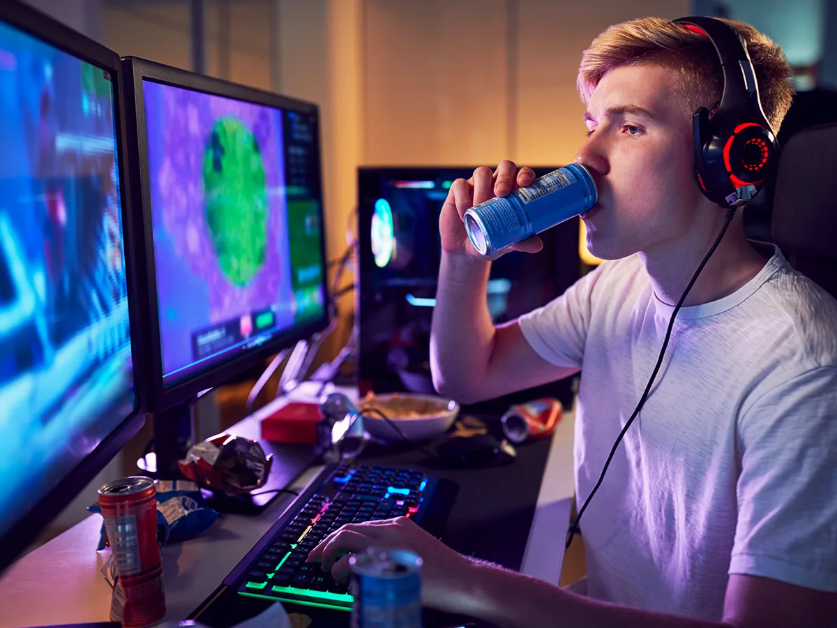 A teen drinks a caffeinated energy drink while playing a computer game. 