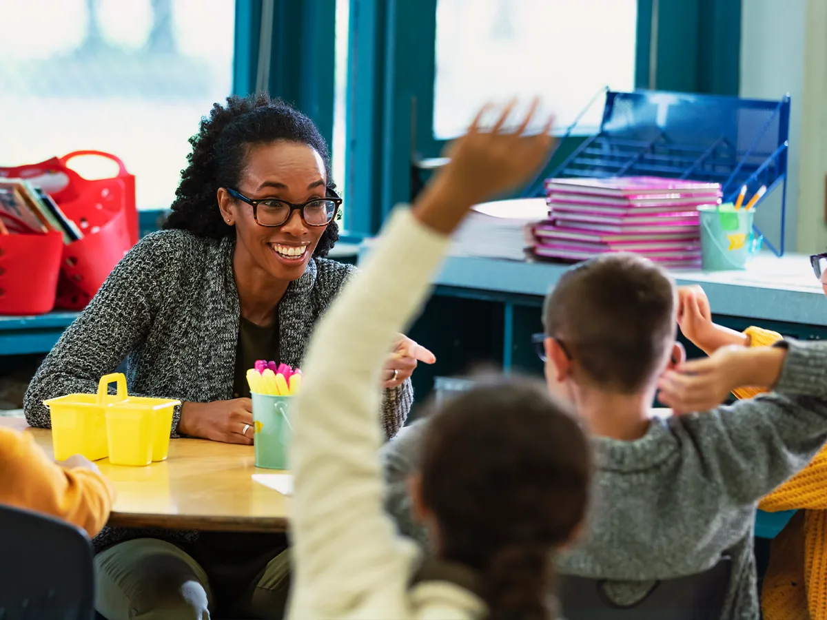 The power of praise: a guide for teachers. A smiling teacher calls on a student in a classroom.