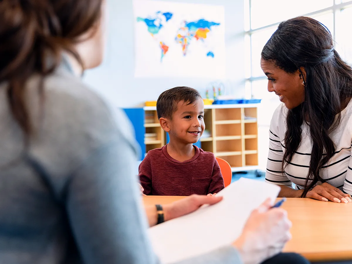 How to tell if your child’s IEP goals are SMART? A young child meets with their parent and teacher. 