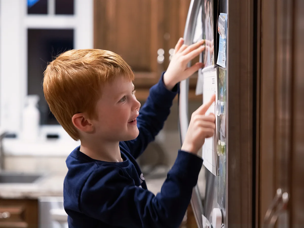 10 tips to help get your child organized. A child points to the calendar on a refrigerator. 