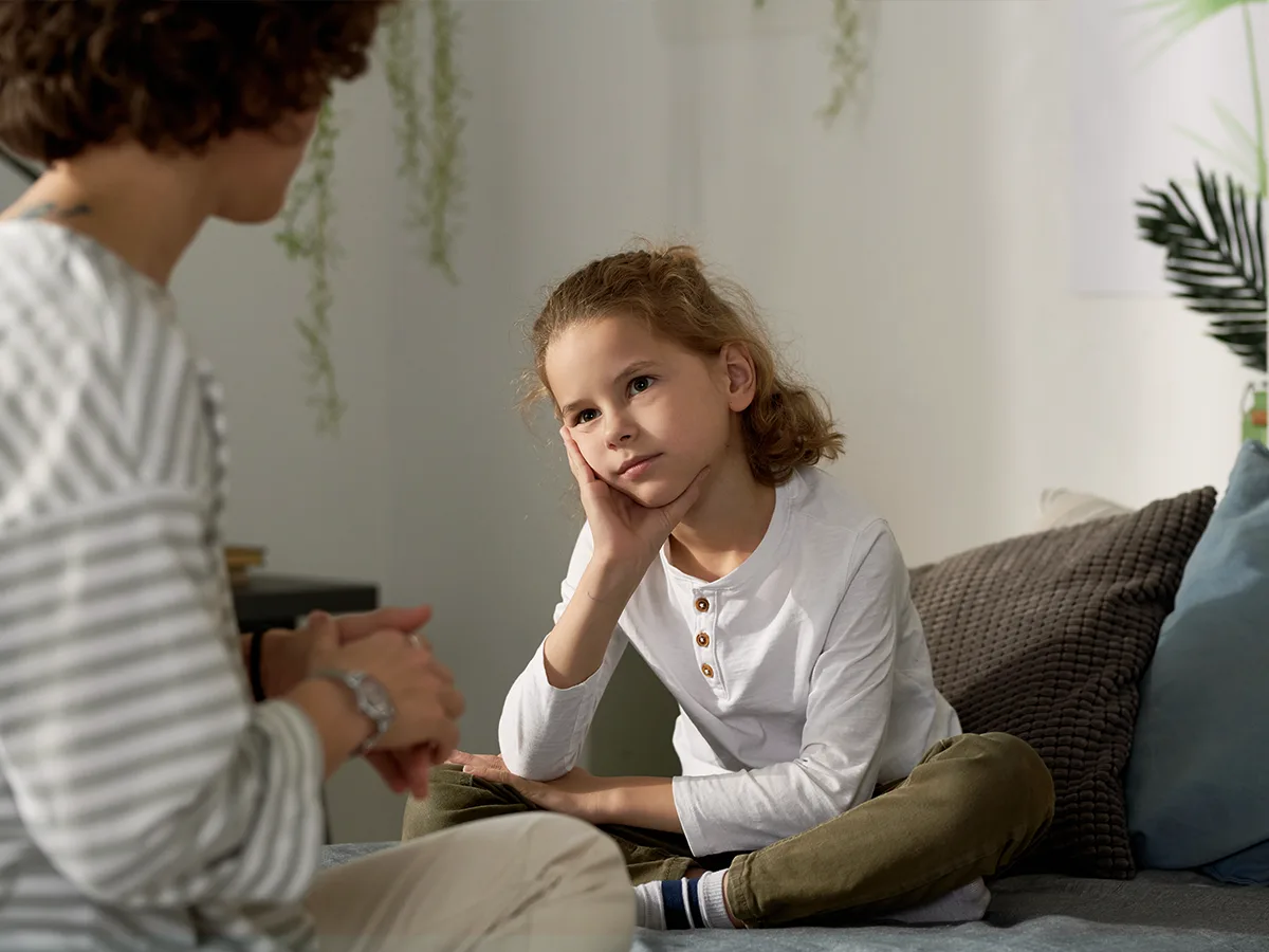 An adult talks to a child who is sitting on a couch. 