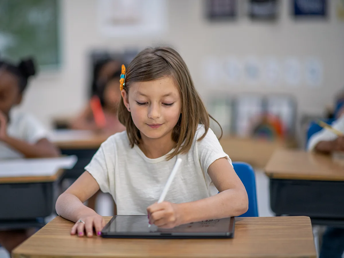 Una niña escribe en una tableta sobre un escritorio en un salón de clases. 