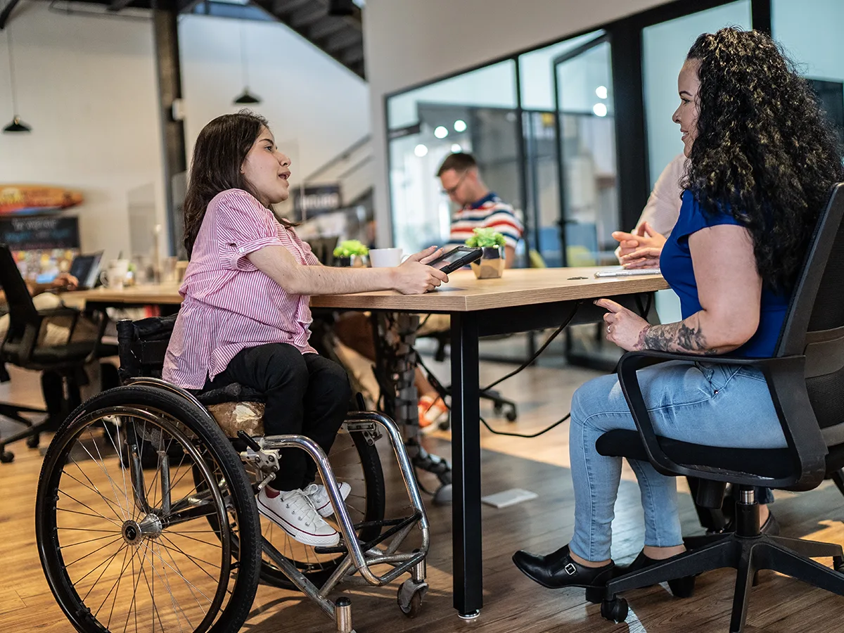Workplace Assessment, woman in wheelchair talking to a female coworker in the office

