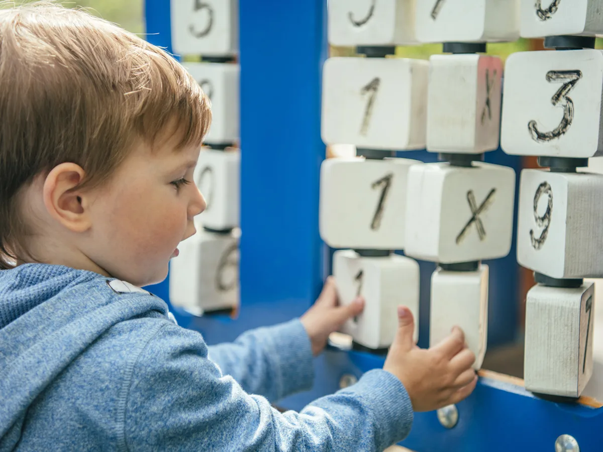 A toddler using both hands to turn over numbered blocks while learning basic math symbols.
