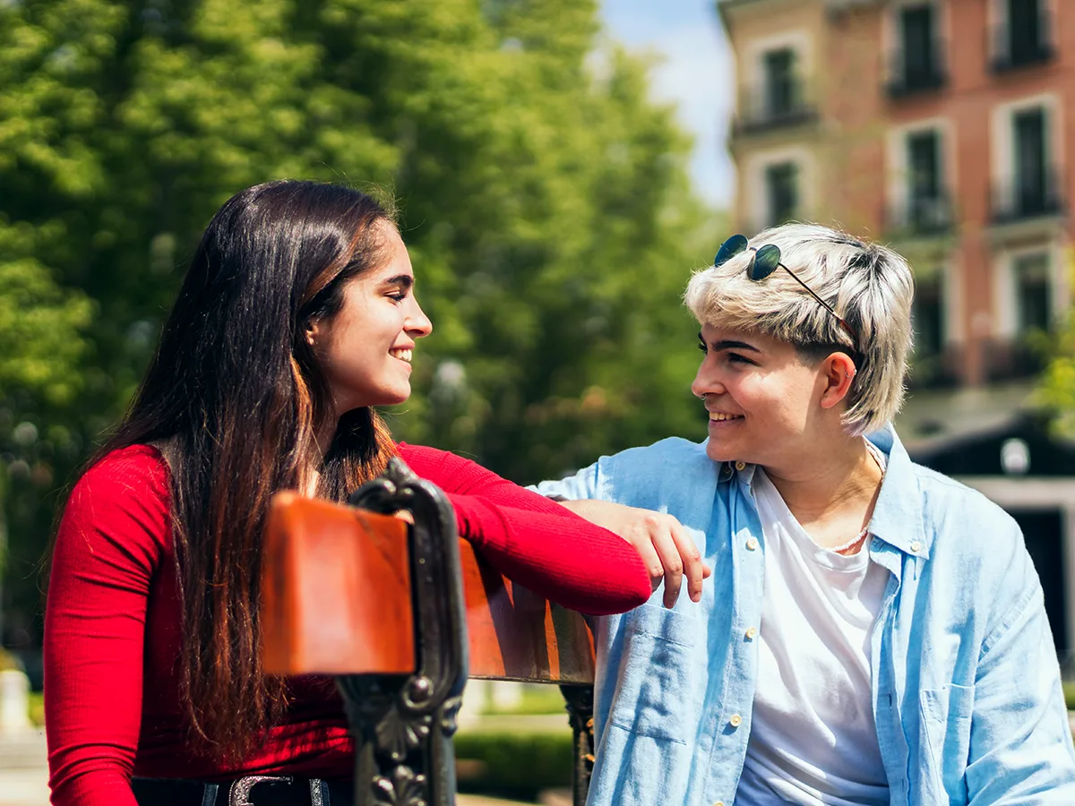 8 ways to help teens with ADHD avoid dating trouble spots. A teenage couple sits outside on a bench, smiling at one another. 