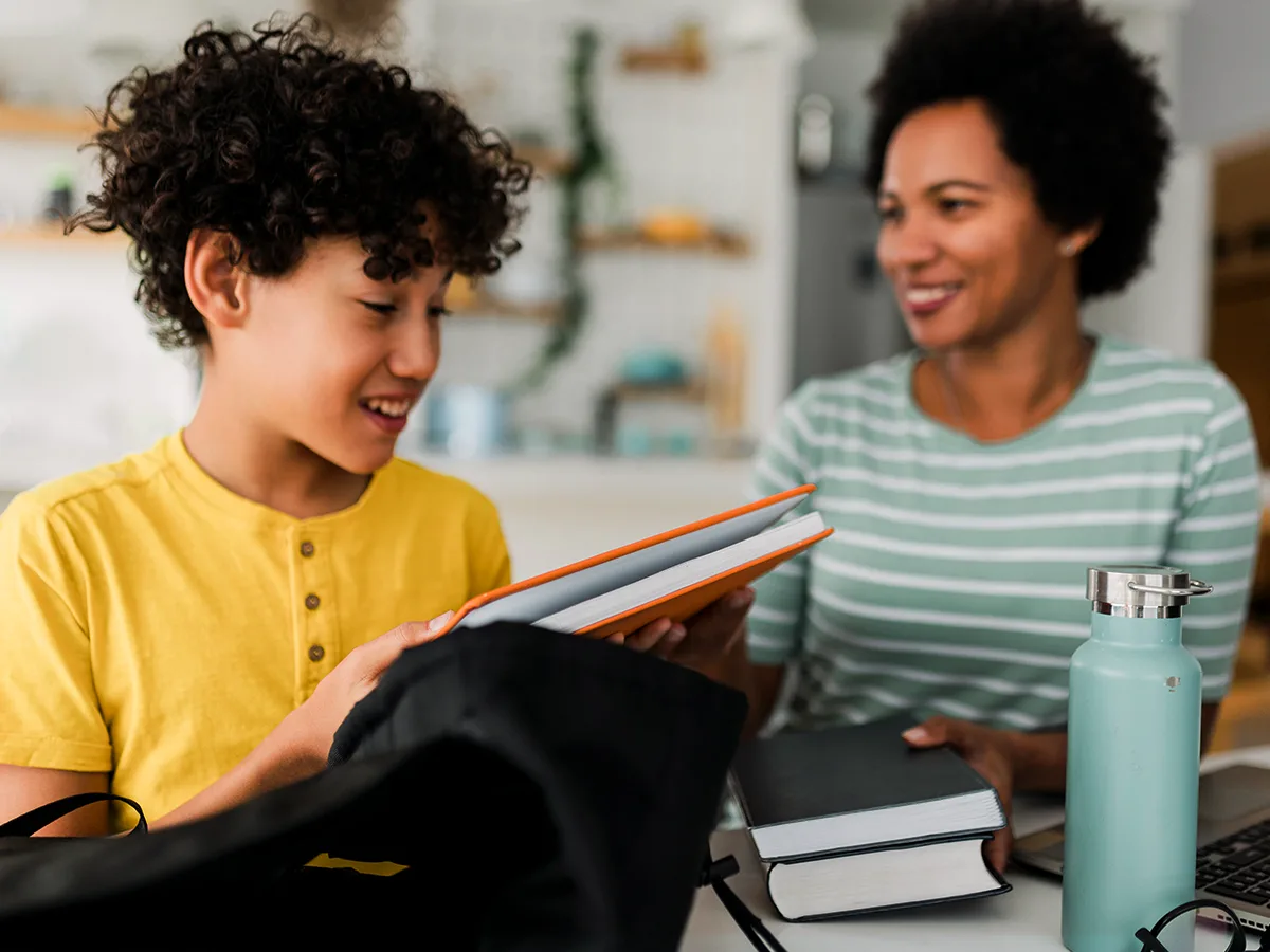 A child smiling with school supplies and an adult smiling at them. 