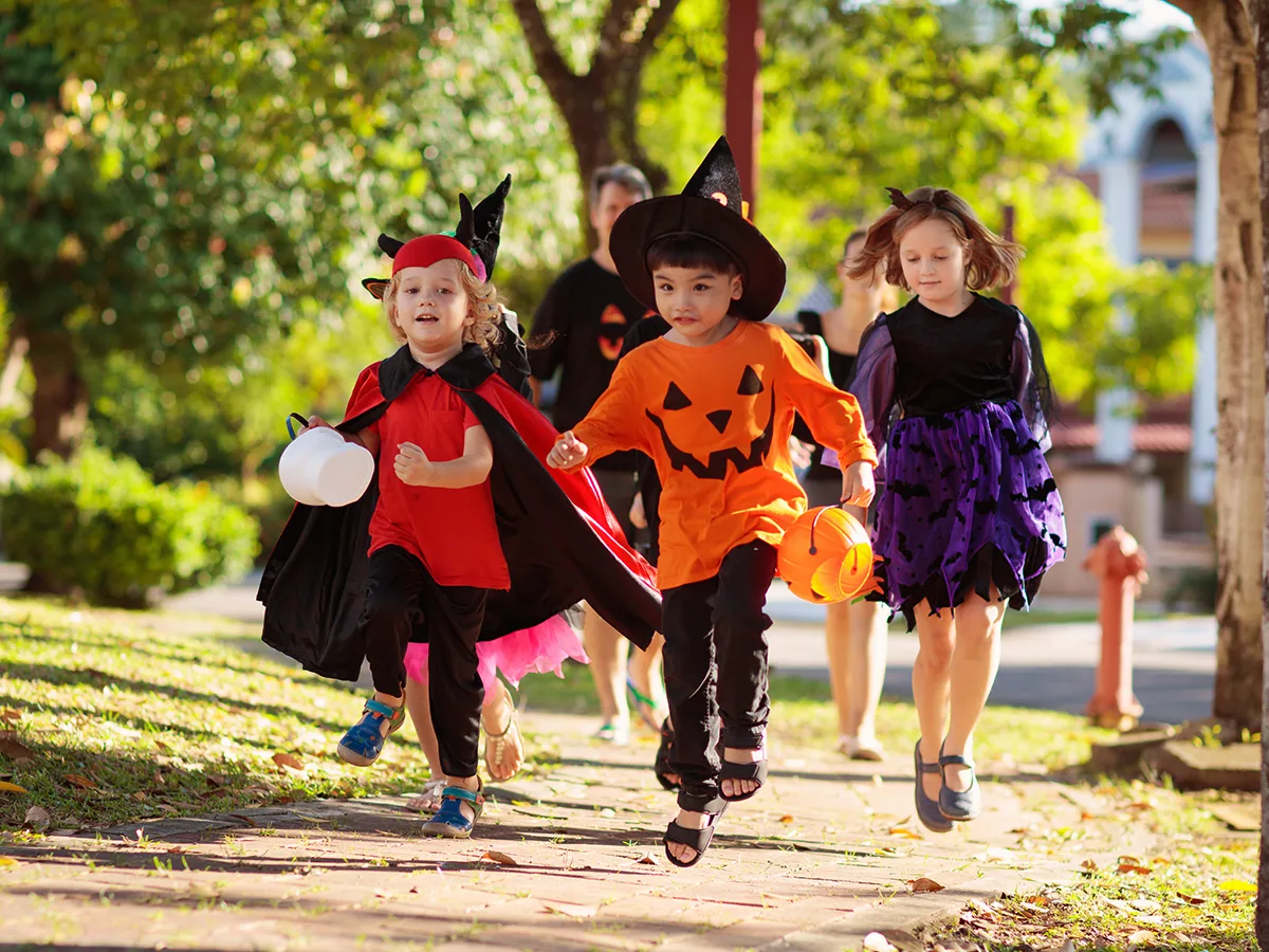 Kids in costumes running down a sidewalk going Trick or Treating. 