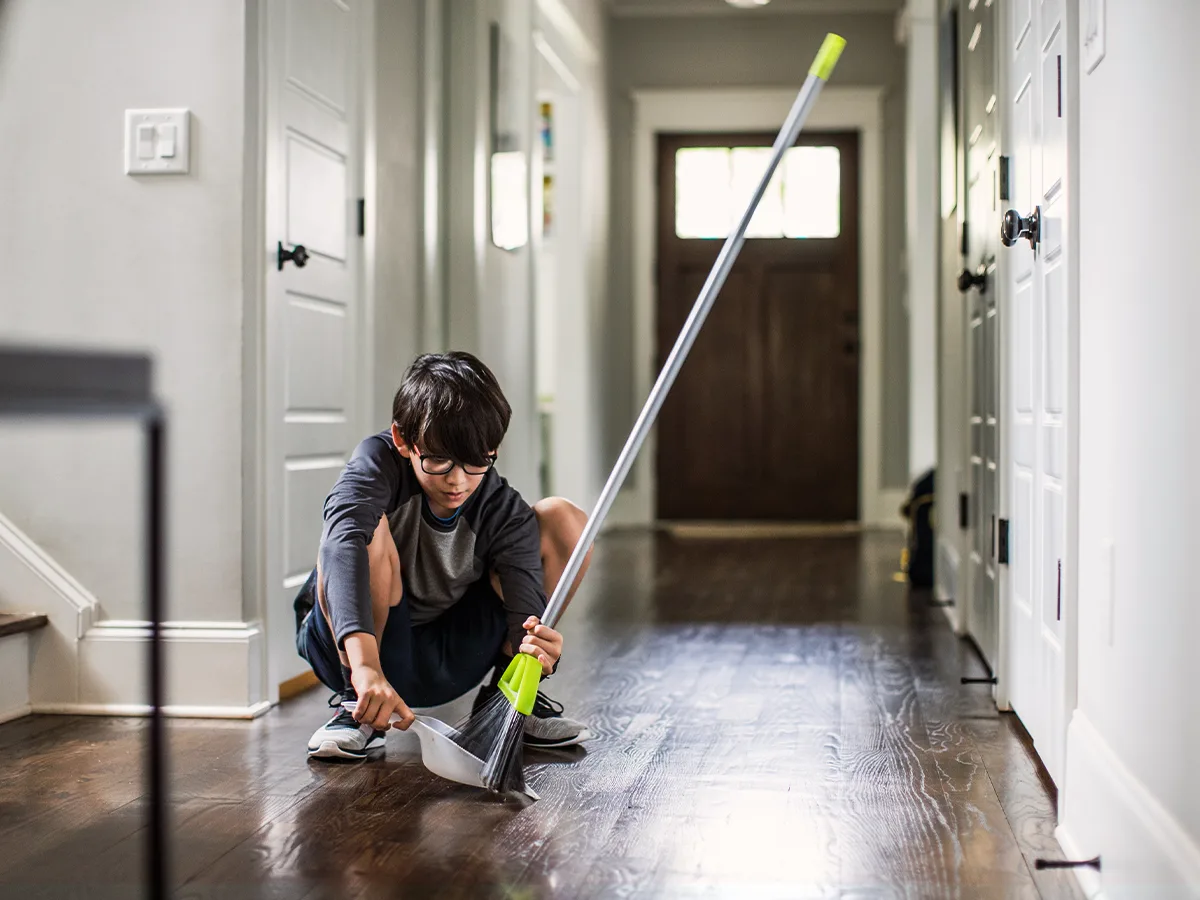 5 tips for helping your child stay on top of chores. A child sweeps dirt in to a dust pan at home. 
