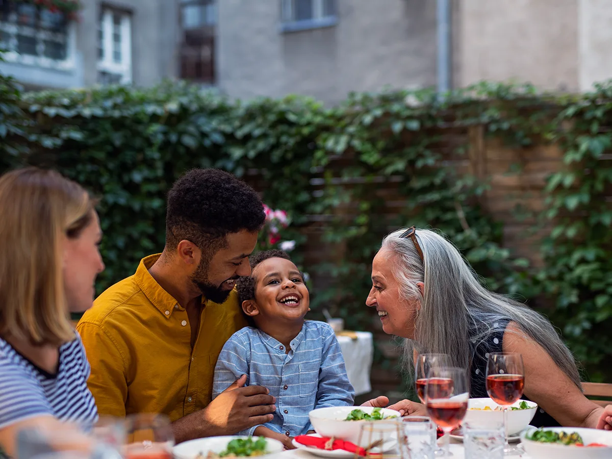 7 ways to prepare kids for visiting relatives and family friends. A child and their family and friends smile at an outside event. 
