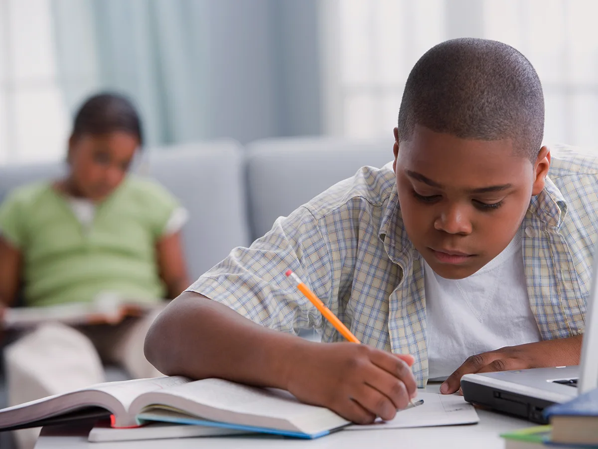 Homework Strategies for Struggling Students. A boy does homework with parent in background.