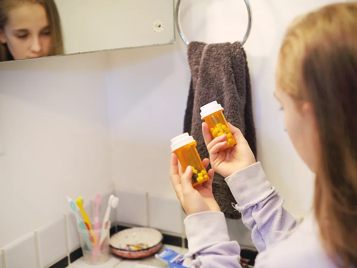 ADHD Medication Misuse, Sharing and Abuse: What You Need to Know, girl holding two bottles of prescription pills, looking down at them in the bathroom
