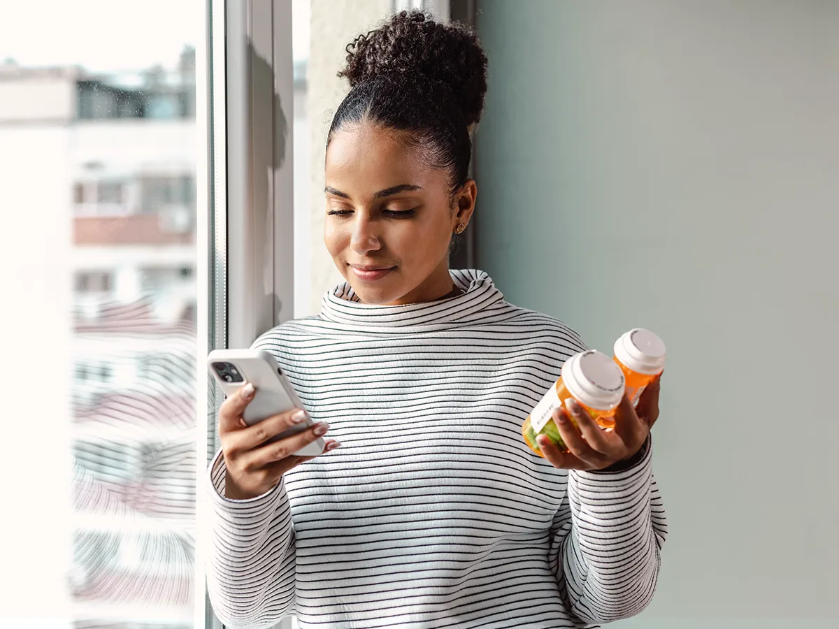 An adult holds two pill containers in one hand while looking at their phone.
