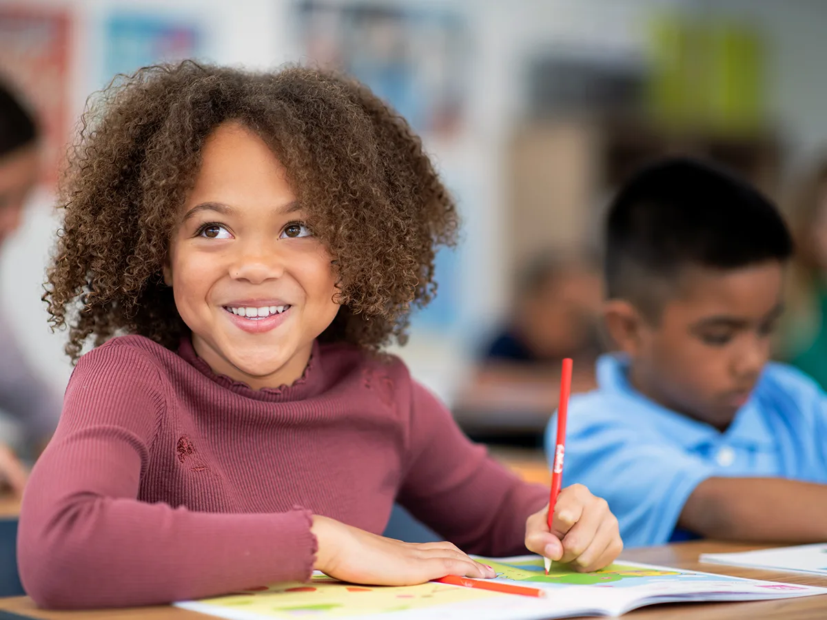 A smiling student writes at a desk. 