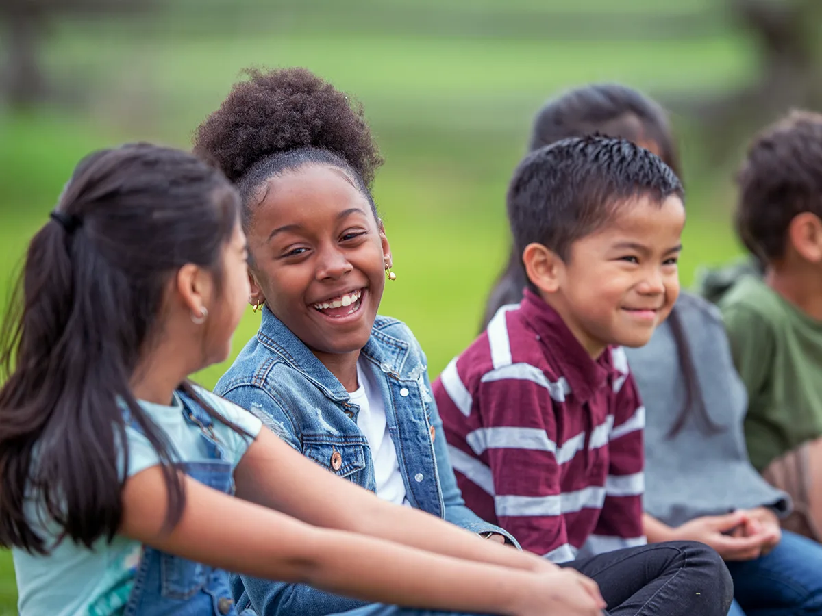 10 ways to help your grade-schooler connect with other kids. A group of children sit outside smiling. 