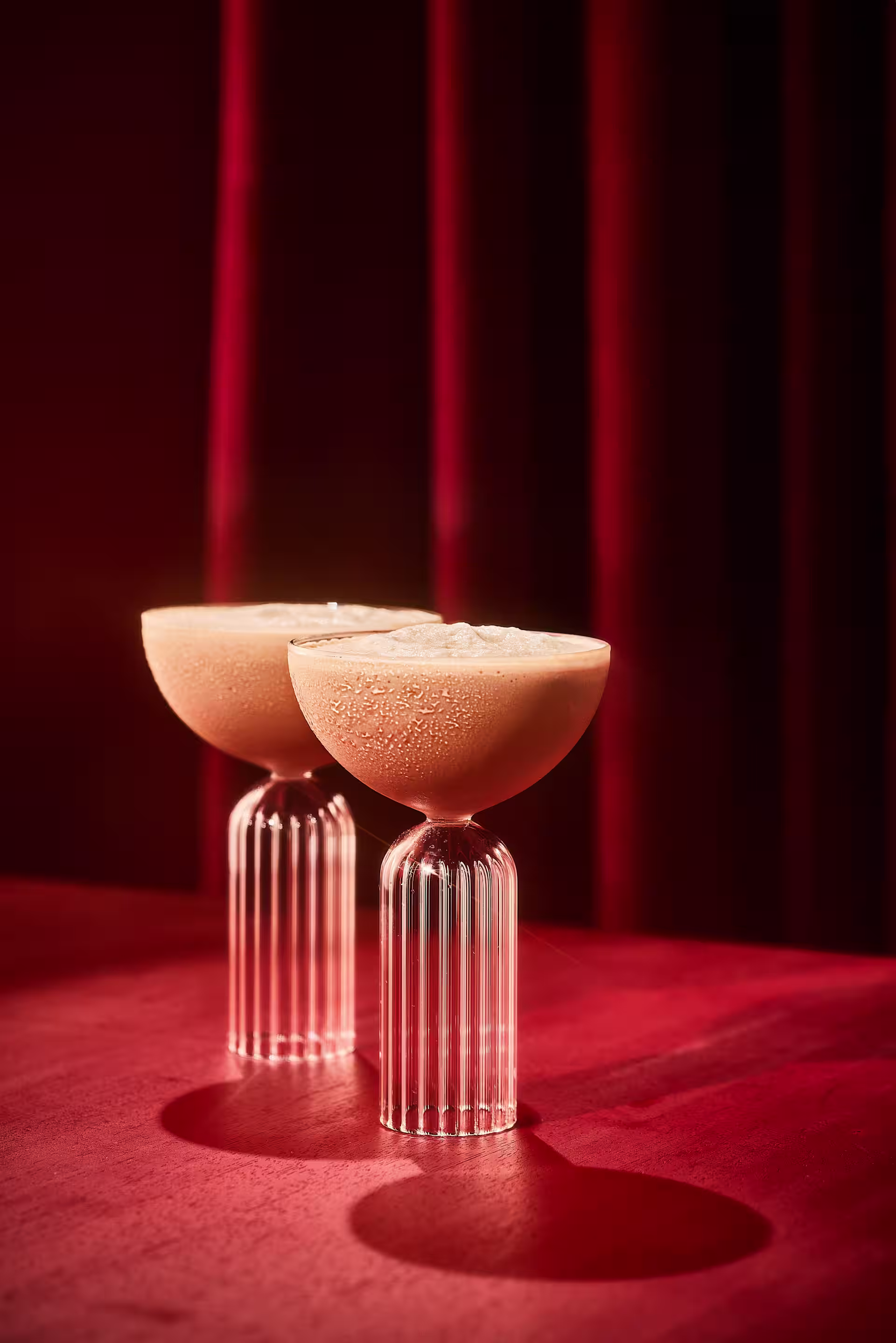 Two cocktail glasses red drape background