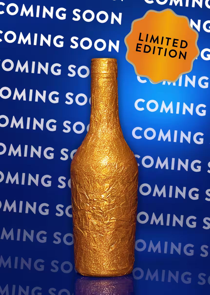 A Baileys bottle wrapped in shimmering gold foil, placed against a vivid blue background with repeated white text reading “COMING SOON.”
