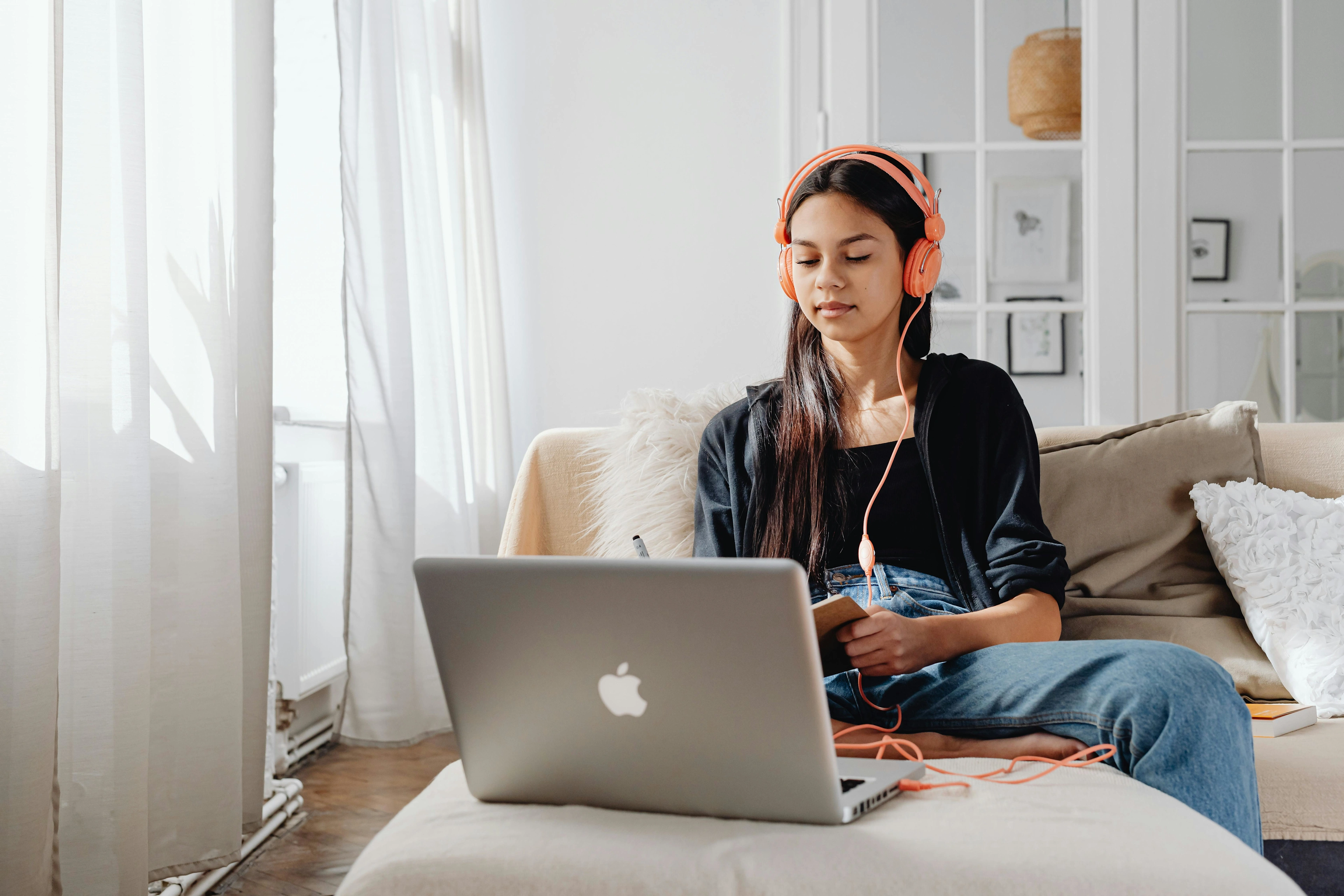A woman sits on the couch with her laptop and headphones on