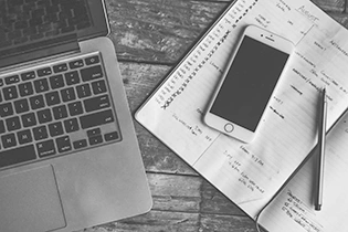 Cell phone lies on a notebook next to a laptop
