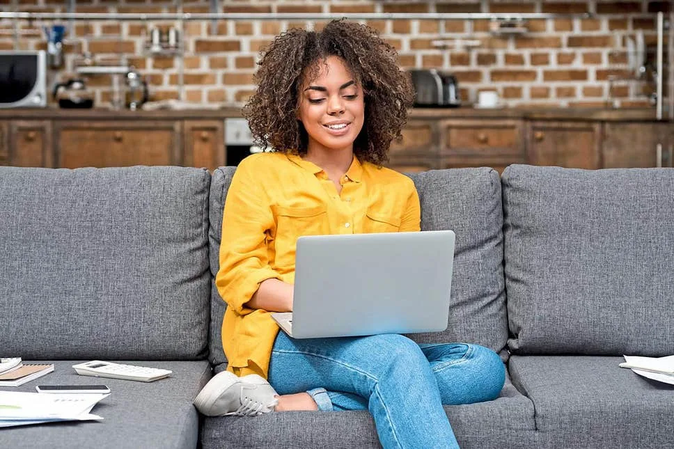 Woman sitting with her laptop on a gray sofa