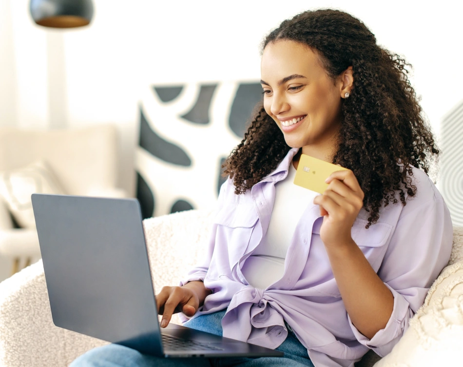 A woman smiling while looking at the computer and holding a credit card.