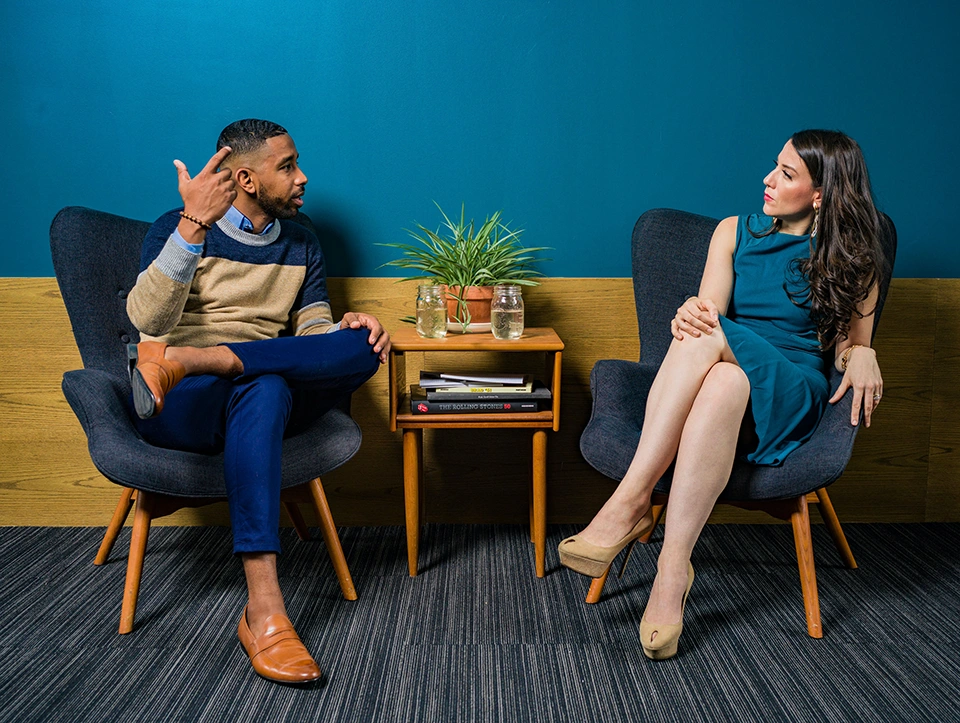 Woman wearing a teal dress sitting on a chair and talking to man