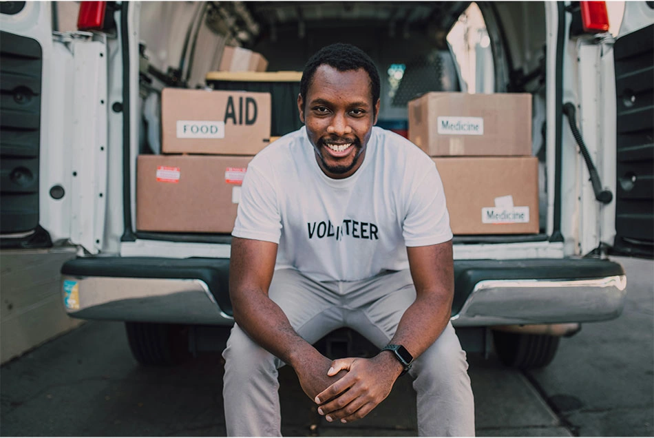 A male volunteer sits on the back of a volunteer truck smiling