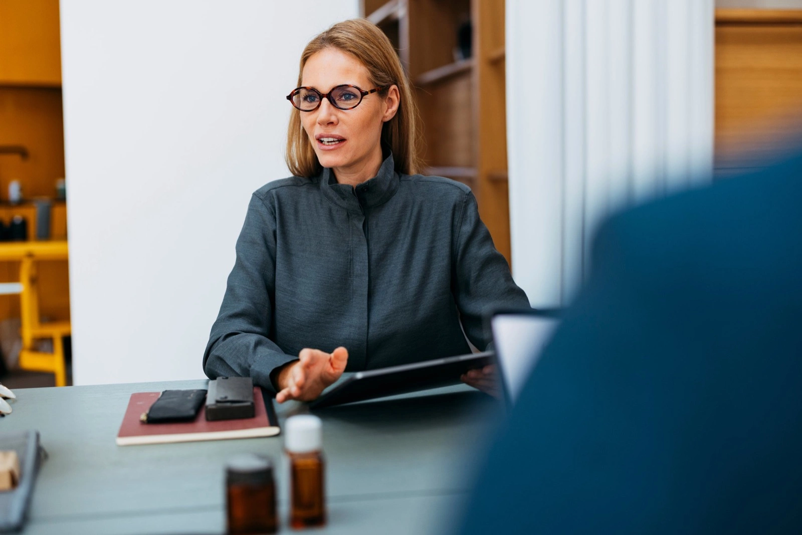 Une femme à lunettes parle de l’autre côté d’une table de réunion, dans un bureau