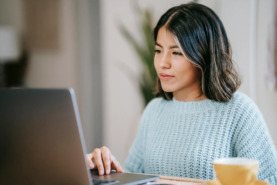 A woman looks at her laptop and is smiling.