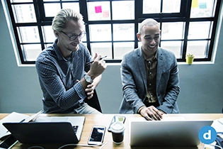 Two talking people sitting next to each other with their laptops.