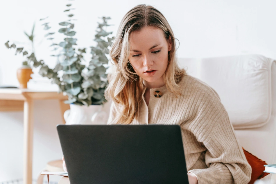 A woman is focused working at home on the sofa or couch.