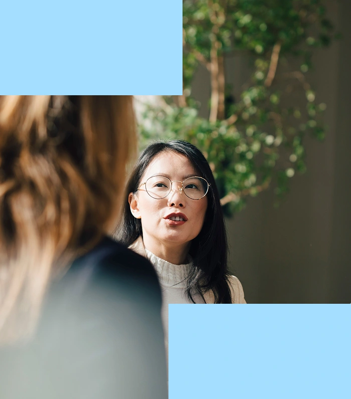 A focus shot on a woman facing another in a one-to-one meeting. The image also has some light blue rectangles around it to emphasize focus on the woman