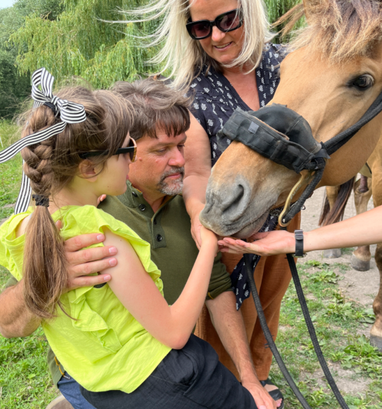 Lucy touching the mouth of a horse with her two parents beside her.