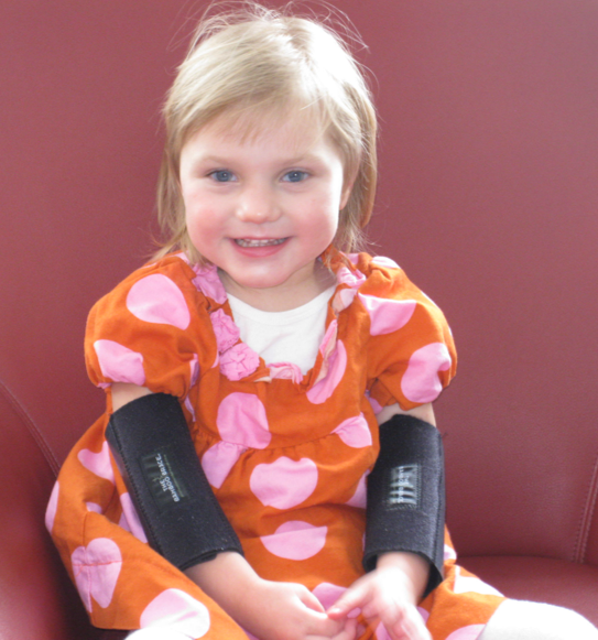 Lucy sitting down, smiling, in a pink, polka dot orange dress.