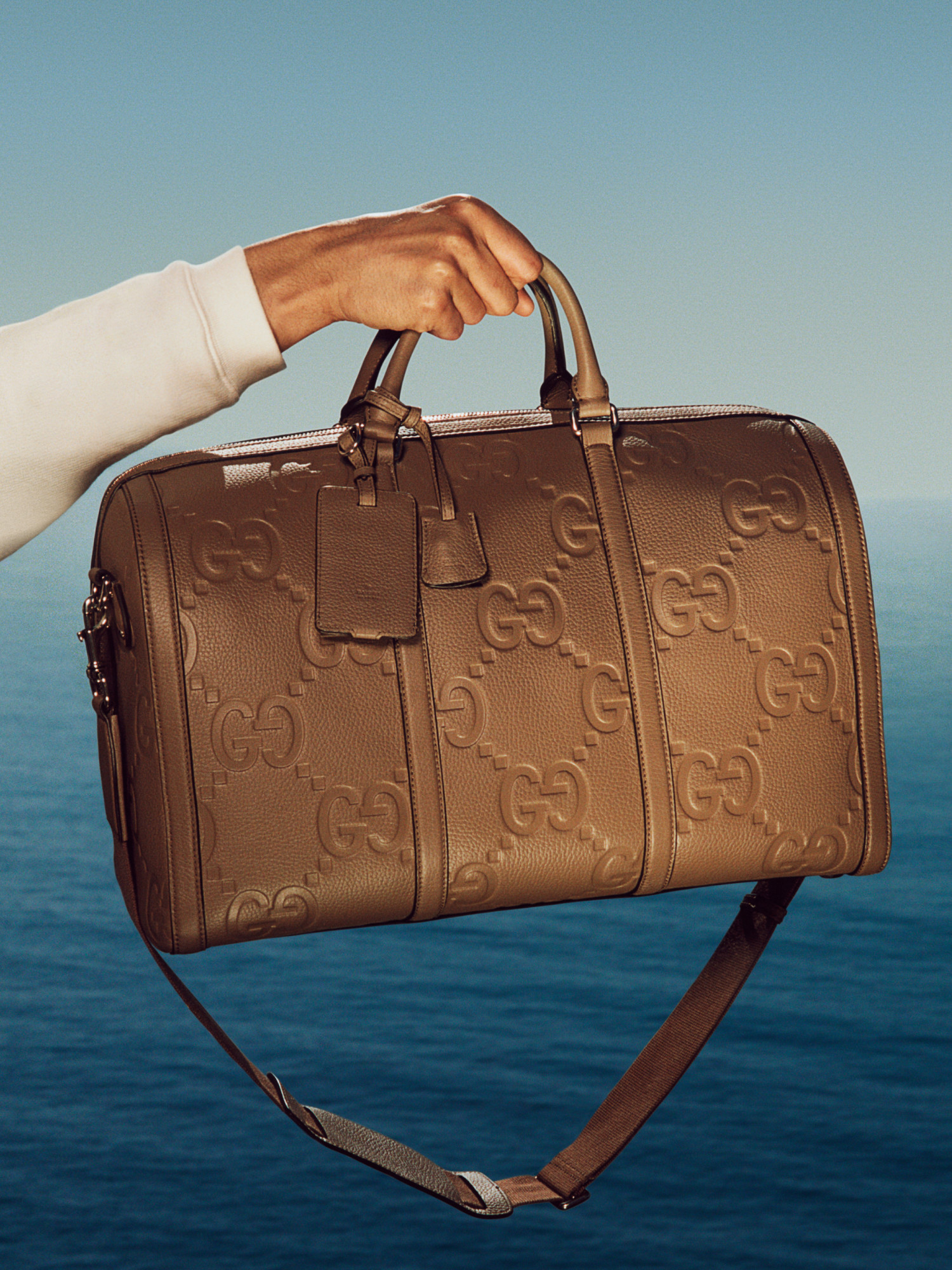 A close-up on a brown duffel bag made from leather with an allover embossed GG pattern.