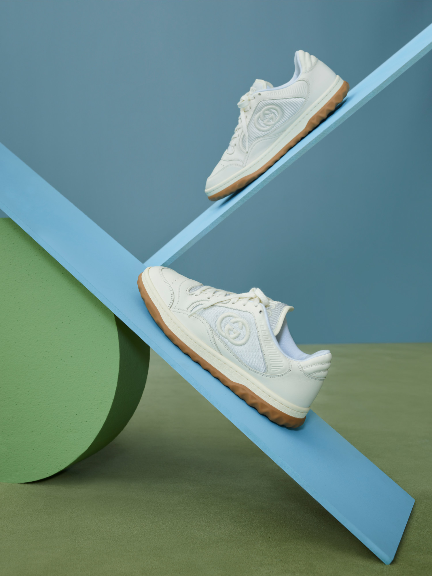 A pair of Gucci Run sneakers in white suede with the Interlocking G logo on a blue see-saw.