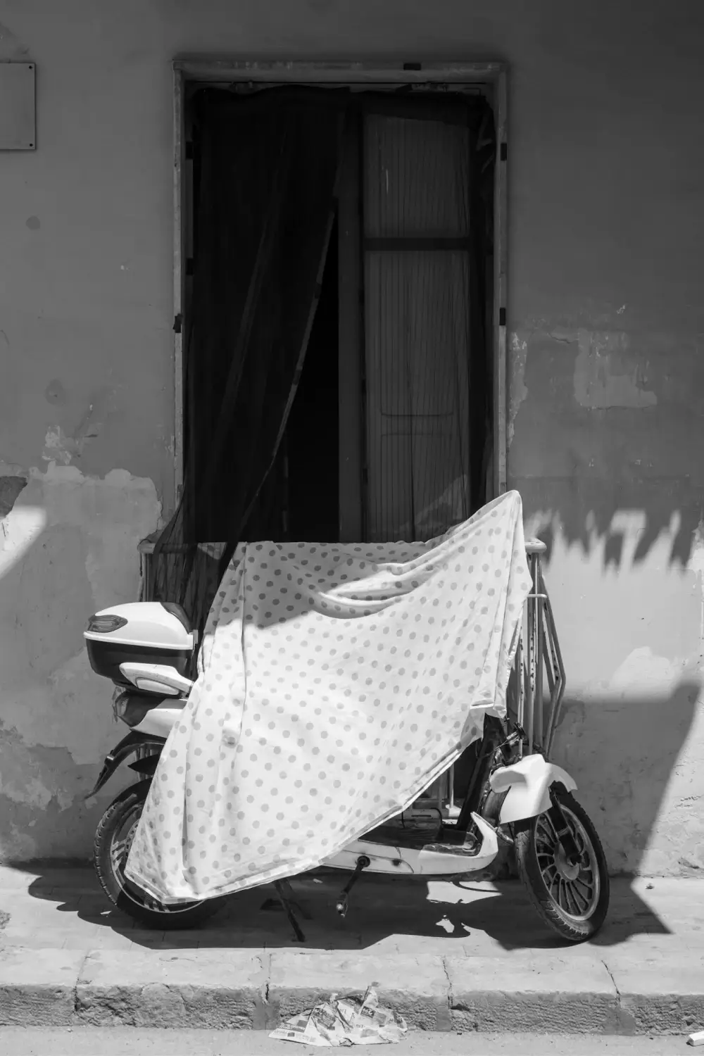 Part of parked motorcycle covered with a sheet of cloth.