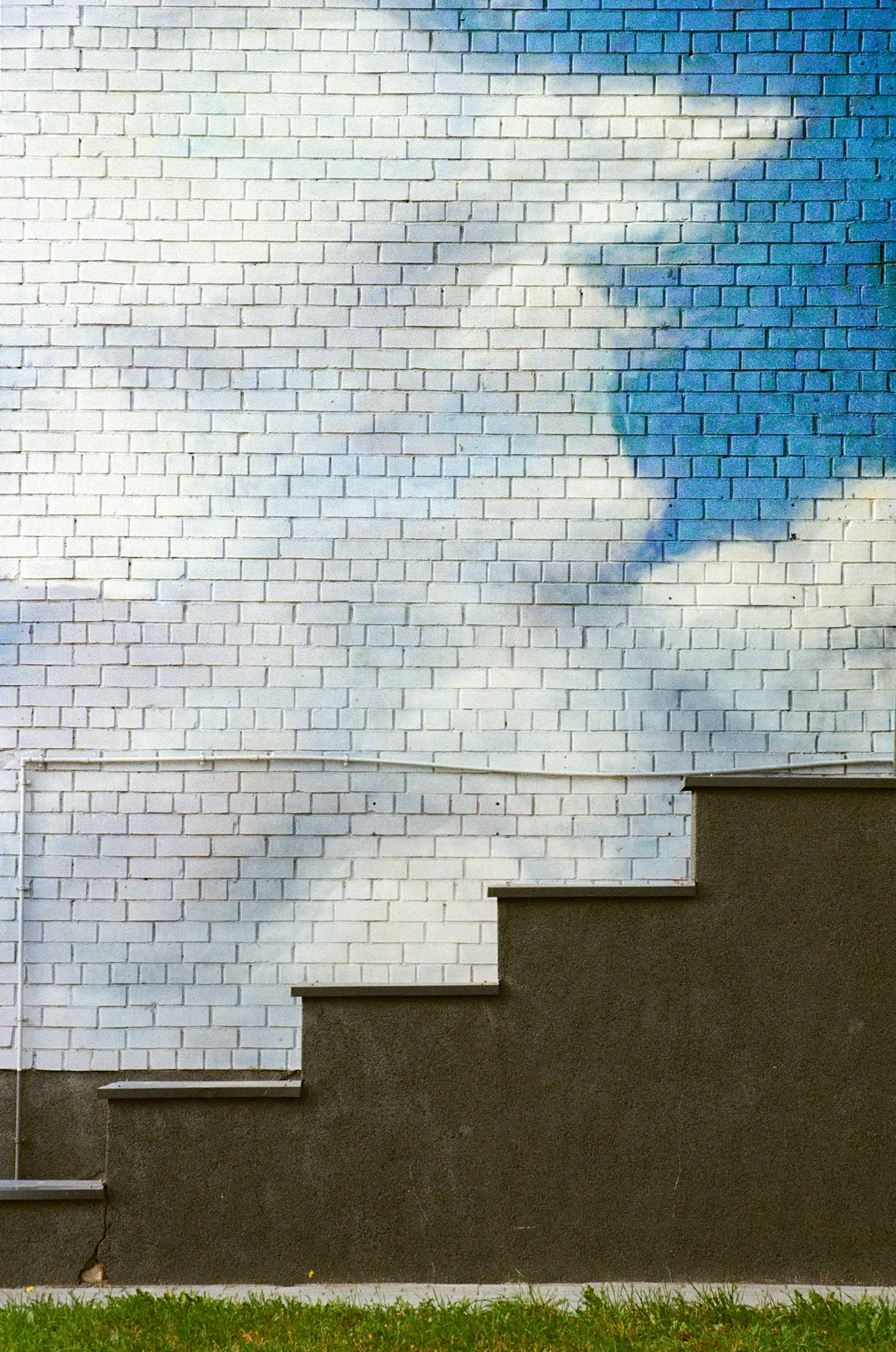 Minimalistic view of a wall painted with clouds and stairs positioned as it looks they climb up.
