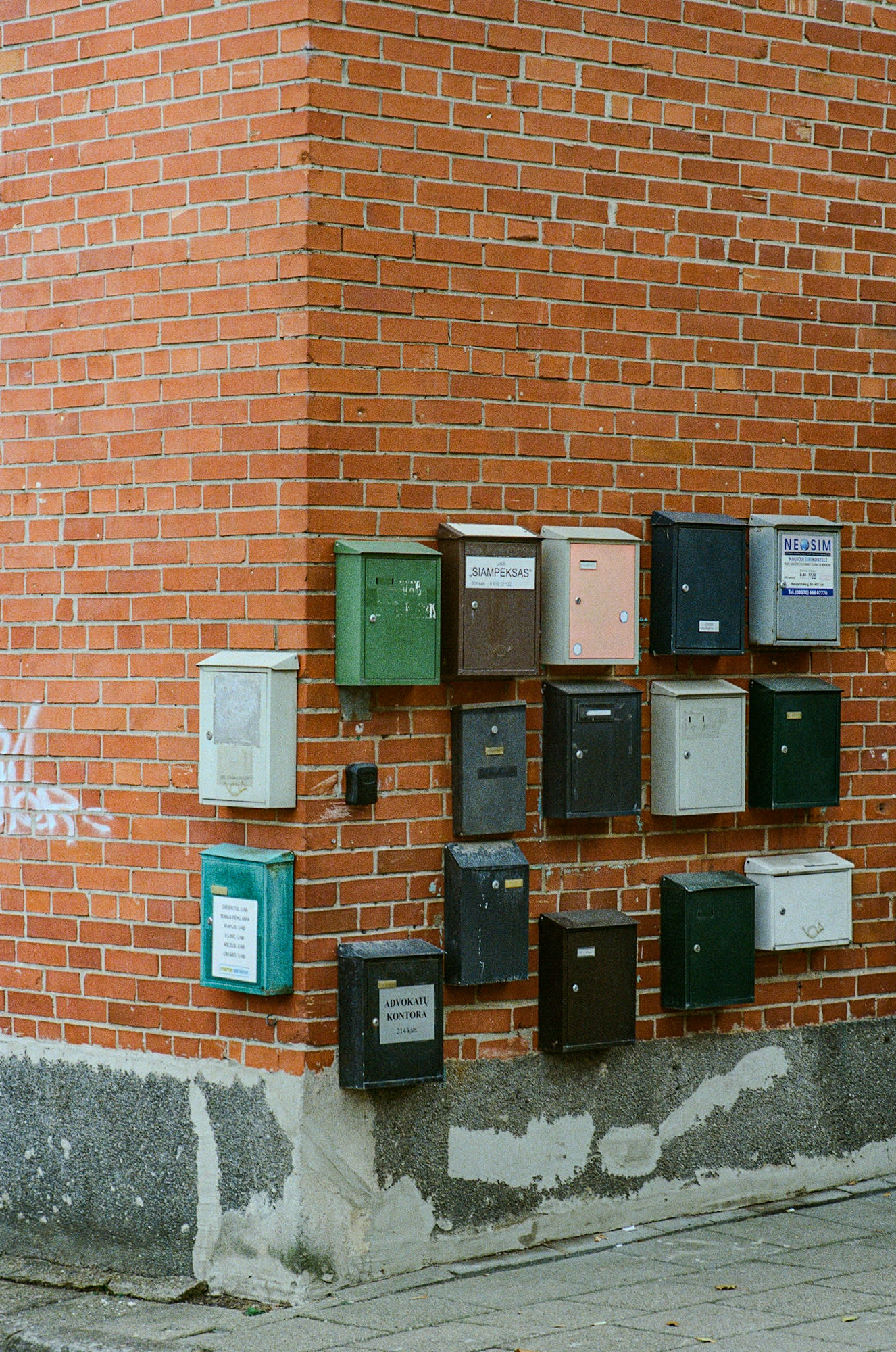 Many letterboxes placed on the red brick wall, and placed neatly on the corner of the wall as well.