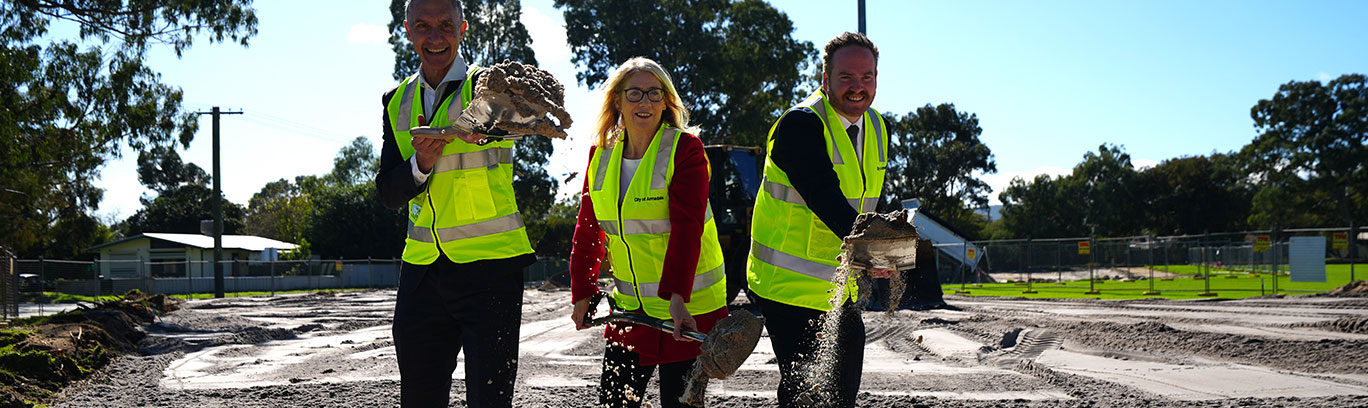 3 people in a construction site wearing high vis throwing dirt in the air with shovels