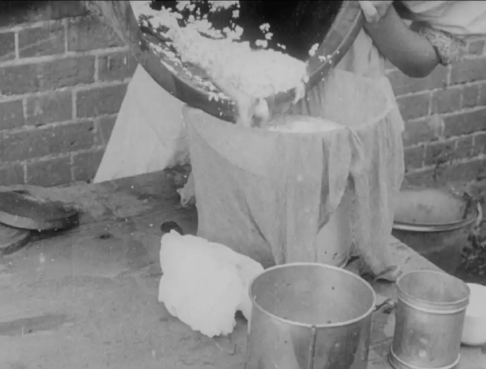 Black and white still from a film, showing a woman churning milk outdoors