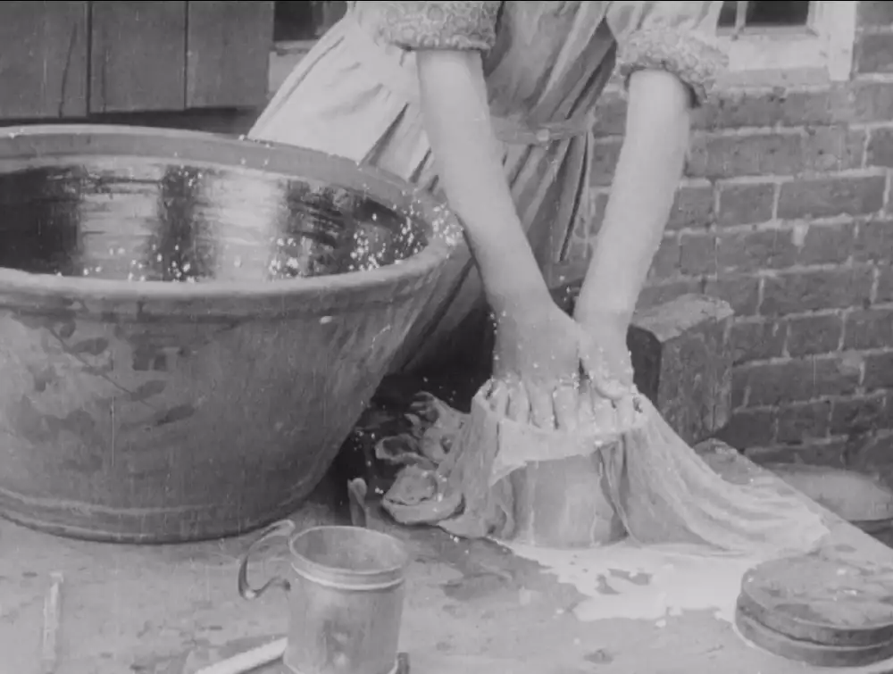 Black and white still from a film, showing a woman churning milk outdoors