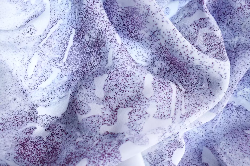 Close up image of a fabric dyed with bacteria. Shows a white fabric with purple spots in an abstract pattern