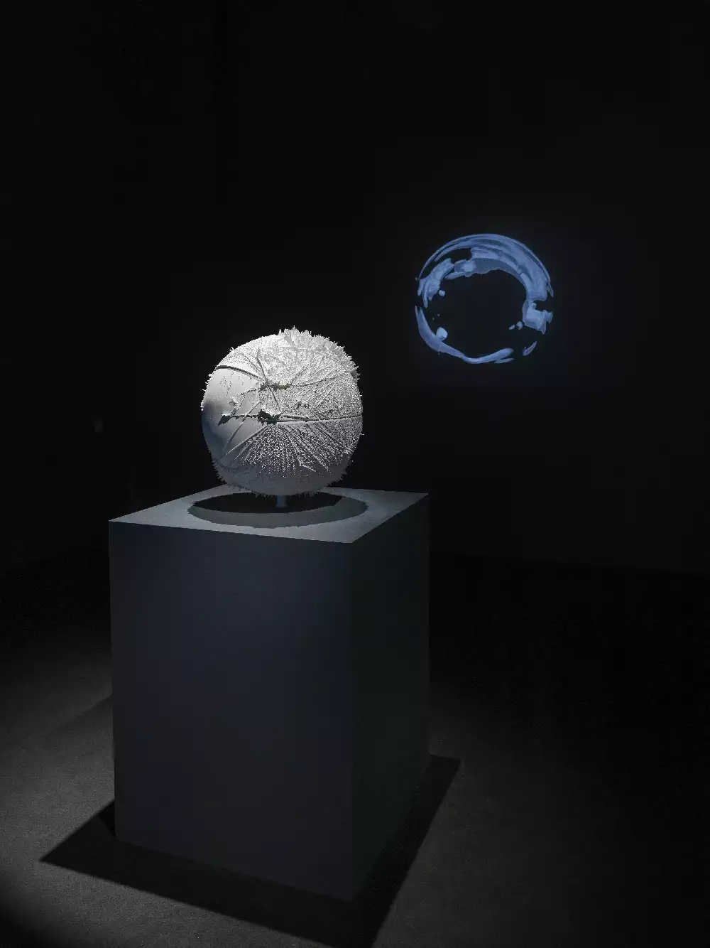 Image of a grey plinth with a white circular sculpture in a dark room