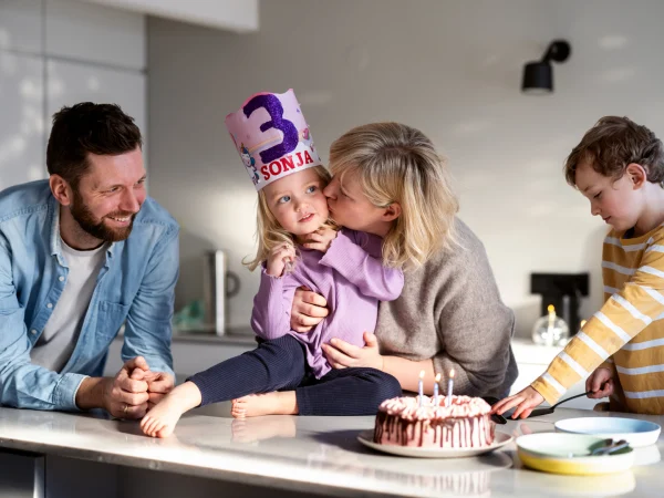 Ei lita jente fyller tre år. Familien har samlet seg på kjøkkenet for å spise kake. 